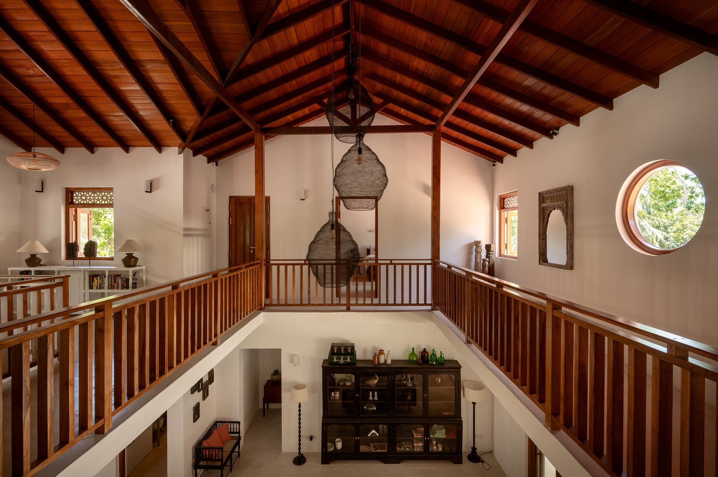 The vaulted teak ceiling and first-floor gallery of the main villa, with wicker lanterns hanging over the living room
